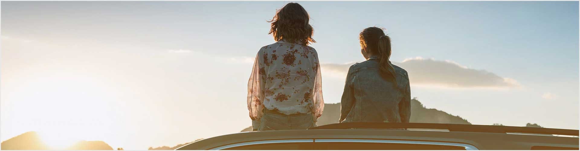 Two women sitting on a car watching the sunset