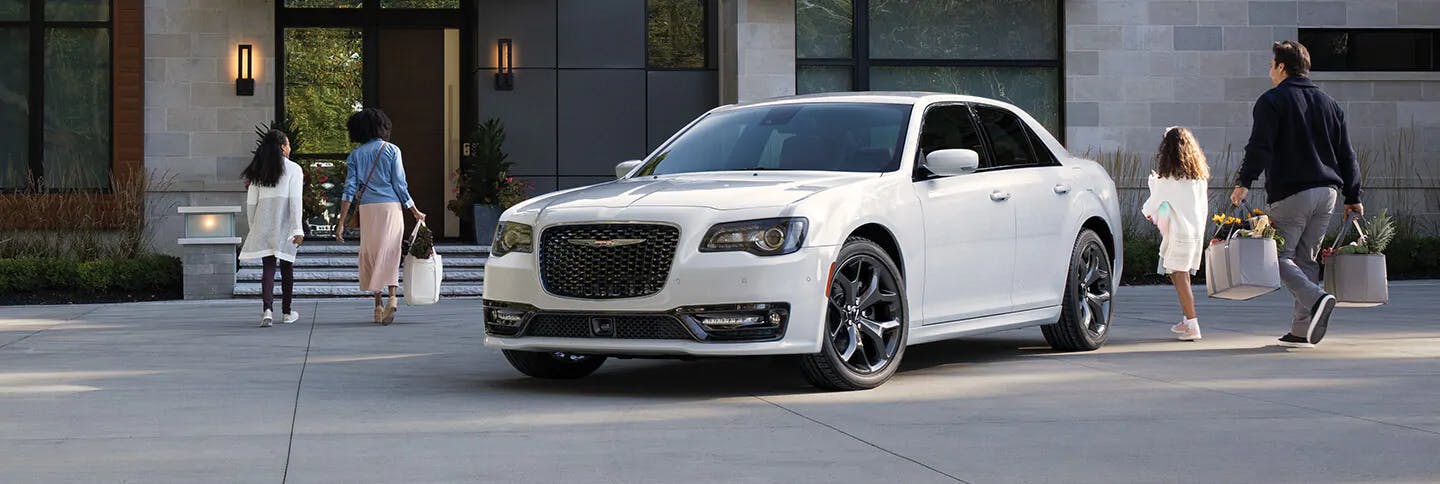 white Chrysler sedan parked in front of a home with a mom and daughter to the left and dad and daughter to the right