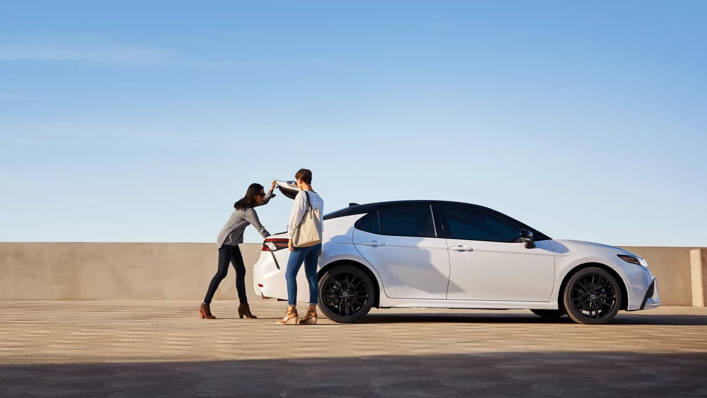 two brunette women unloading the trunk of a white Toyota Camry sedan