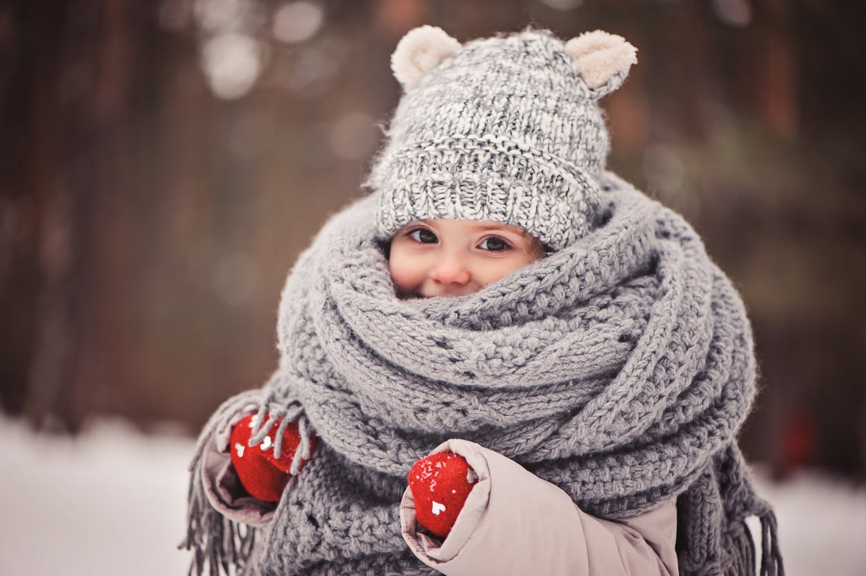 dreamy cozy outdoor portrait of toddler child girl in winter, wearing red gloves, grey knitted hat and scarf