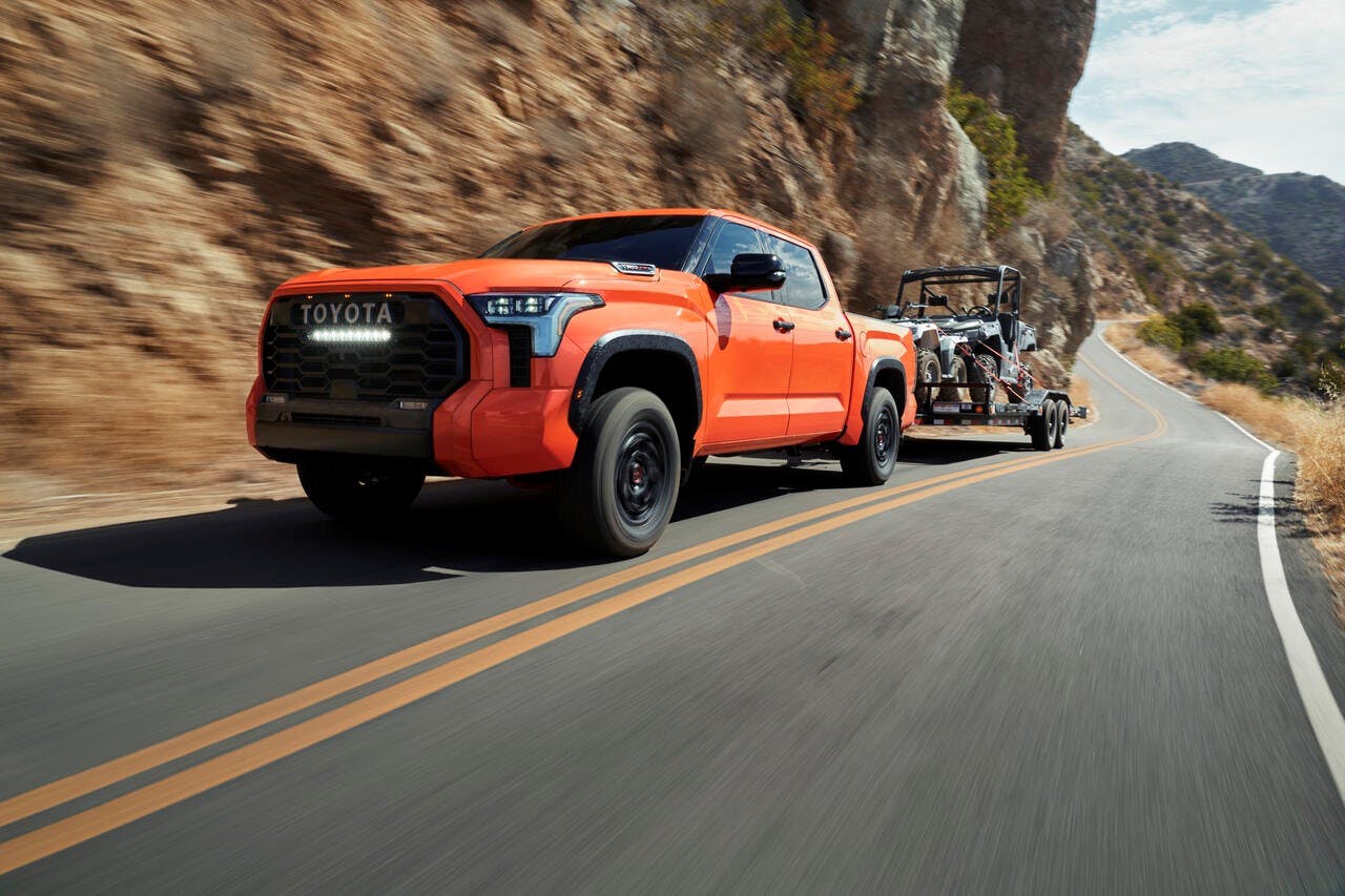 orange 2022 Toyota Tundra pulling ATV on open road by mountains