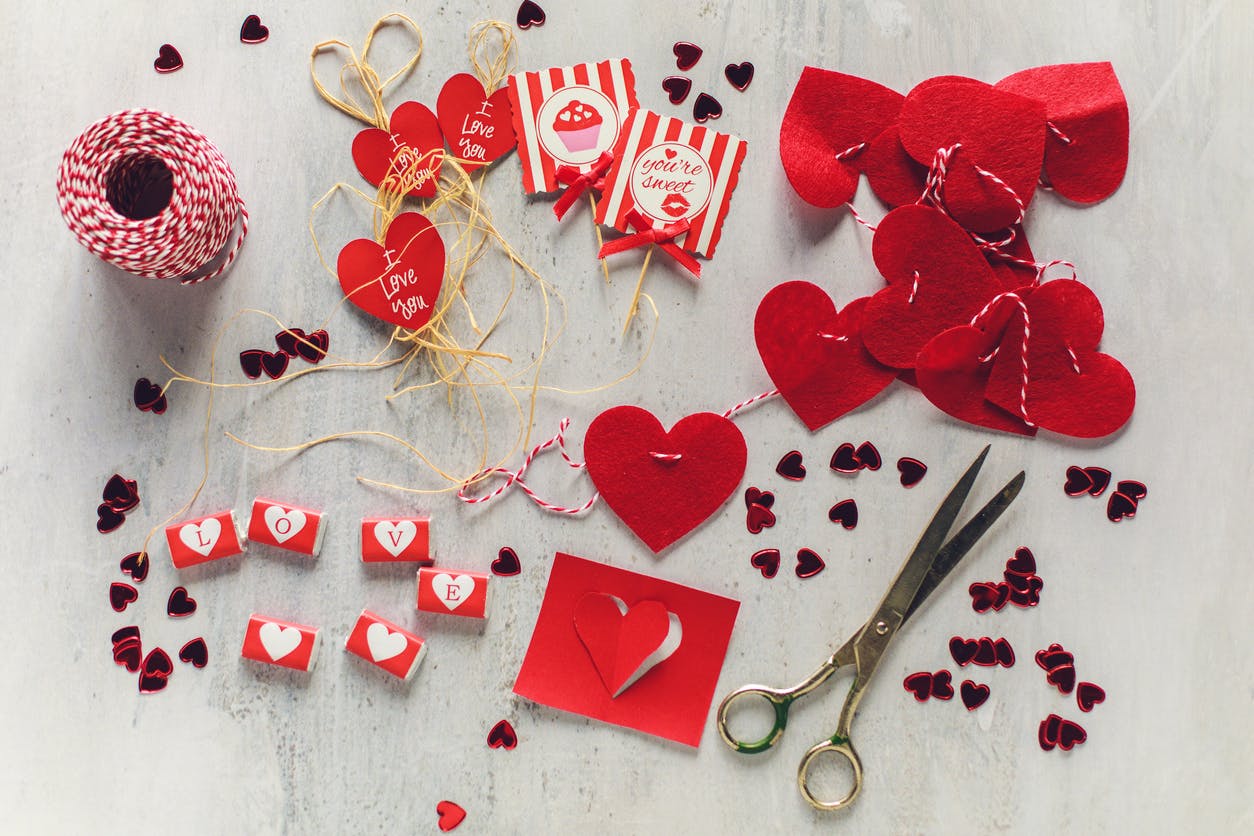 Directly above of a gray table with decorative elements like cards, cords and candies that someone is cutting for Valentine's Day.