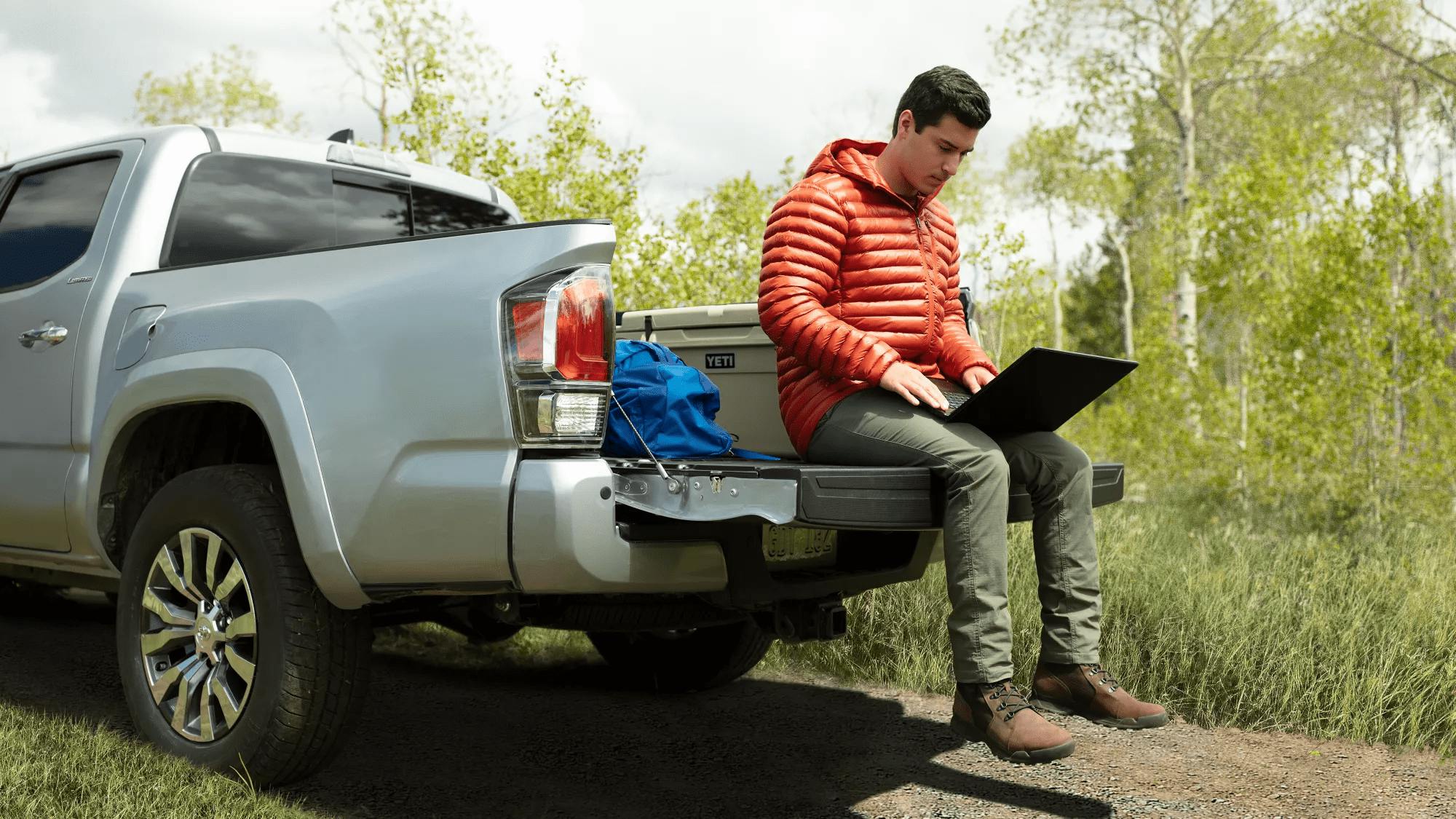 man sitting in bed of toyota tacoma on laptop