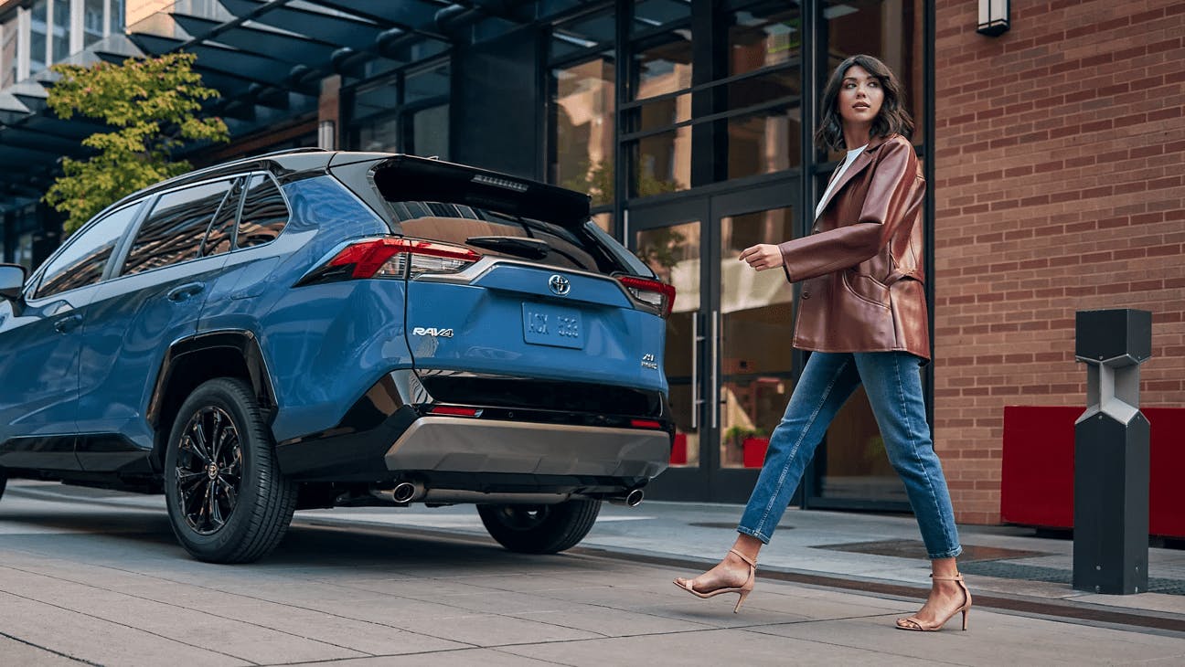 woman walking behind parked blue 2021 rav4 hybrid 