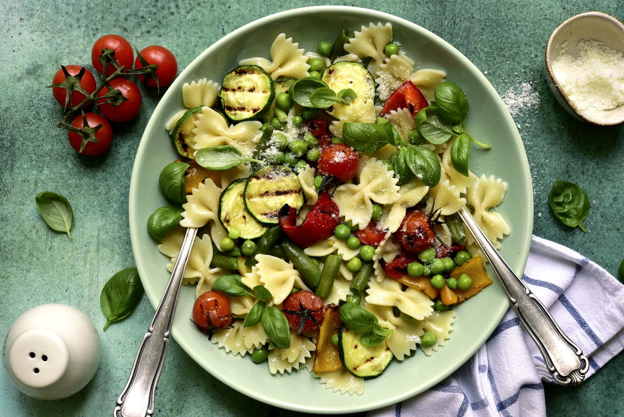 traditional pasta primavera dish in a bowl over green slate, stone or concrete background.