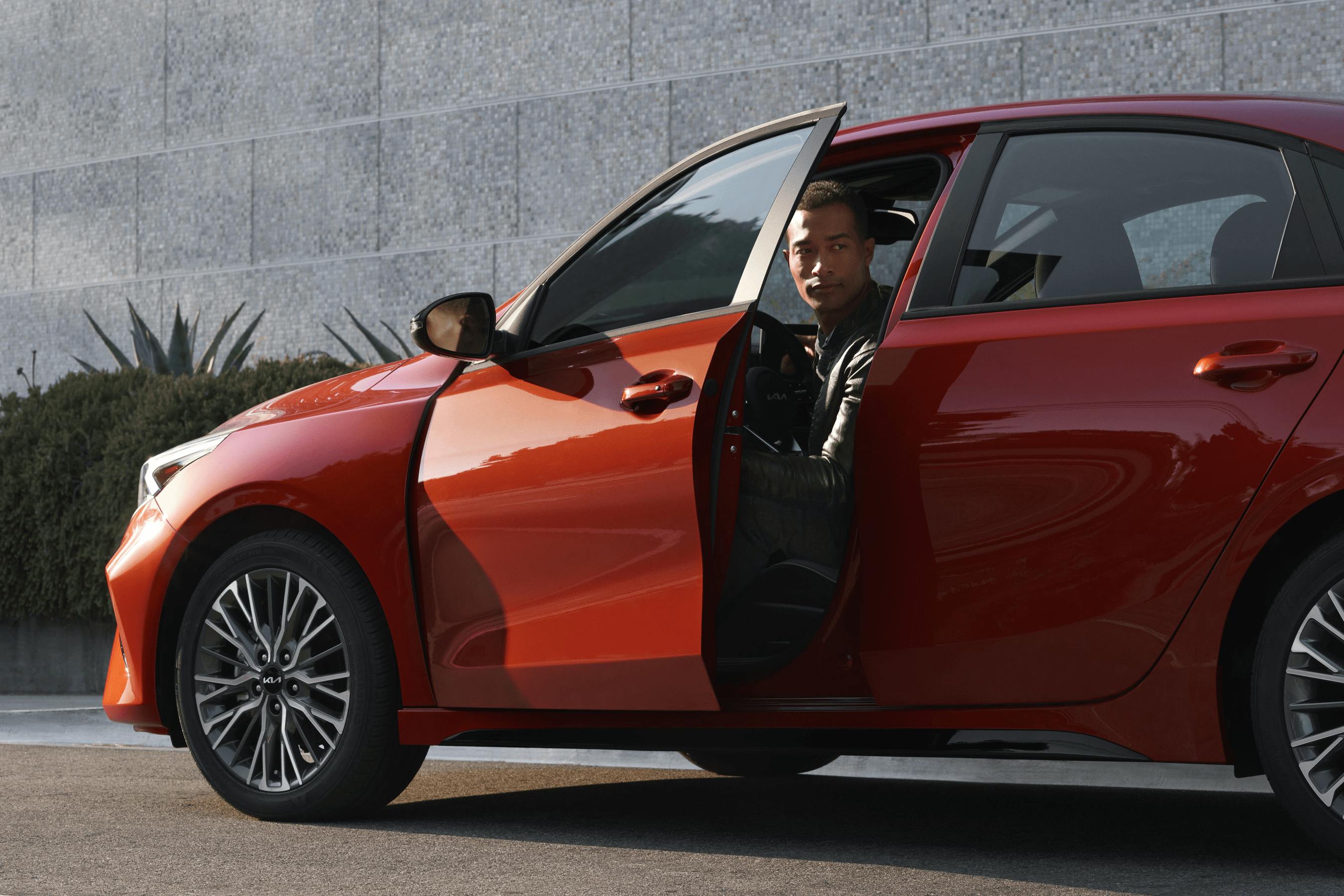 man opening the door of red kia forte