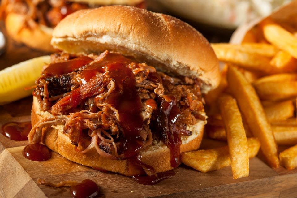 Barbeque pulled pork sandwich and fries on wooden board