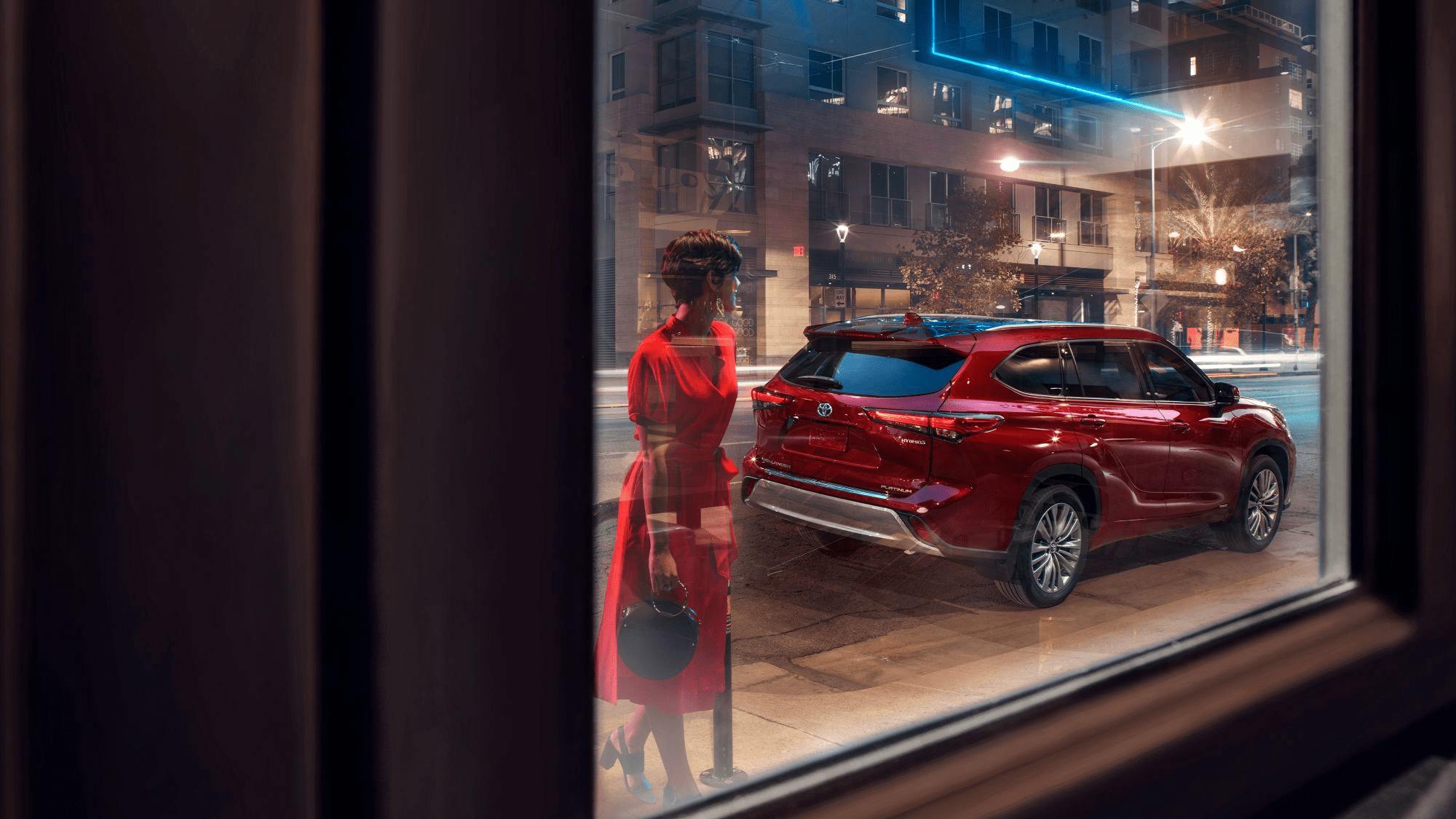 woman in red dress looking through a store window with highlander car in the background