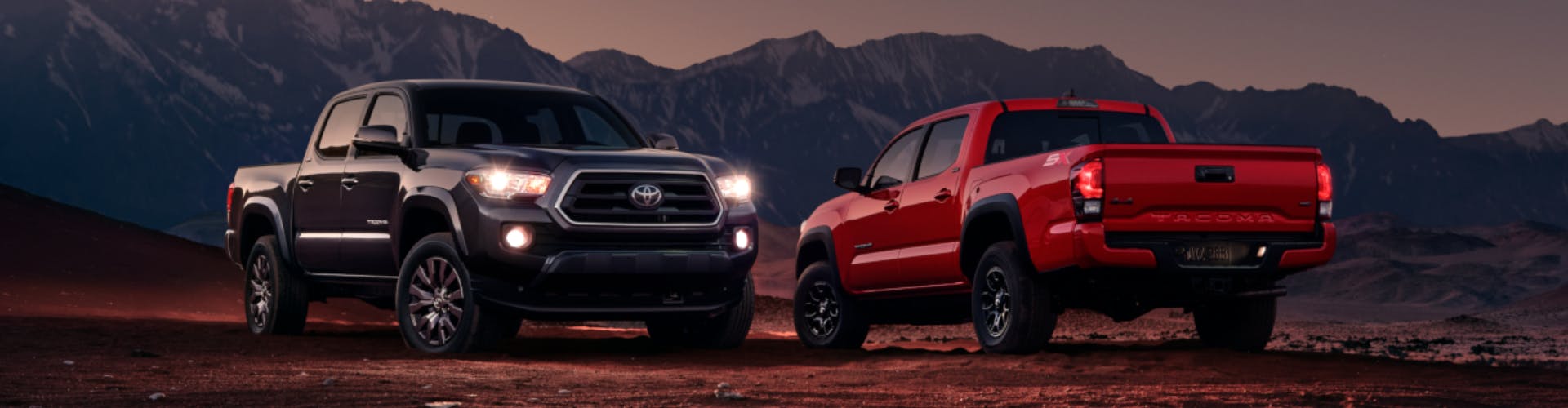 Black and Red Toyota Tacoma trucks parked in front of mountains