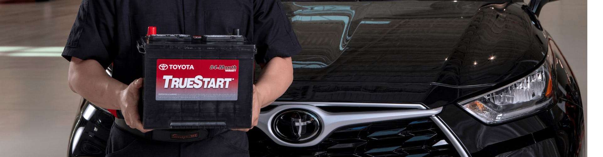 Toyota technician standing in front of black vehicle holding a battery