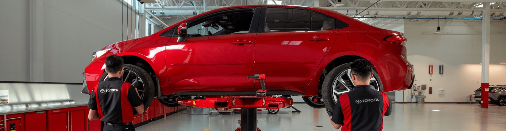 Toyota service technicians replacing tires on red sedan
