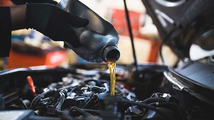 tech pouring oil into a vehicle