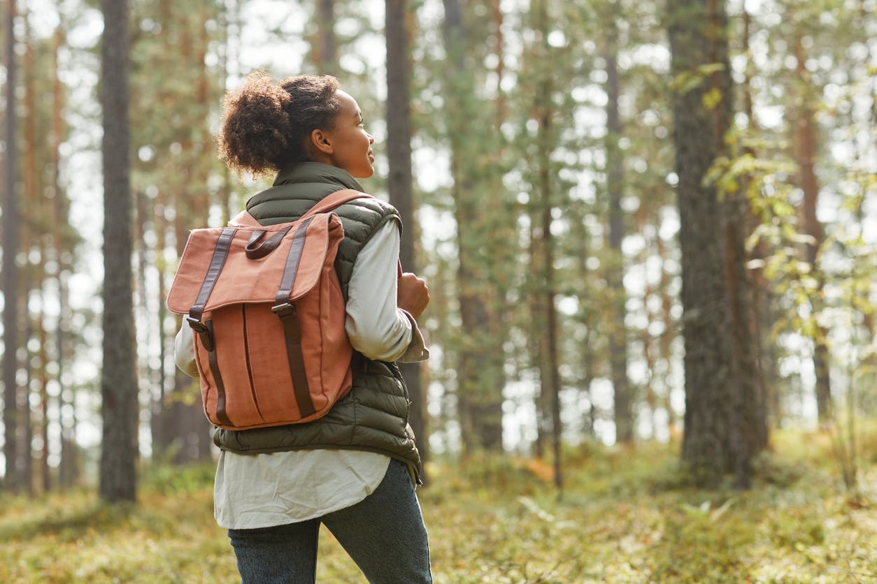 Back view of young black woman with backpack enjoying hiking in forest