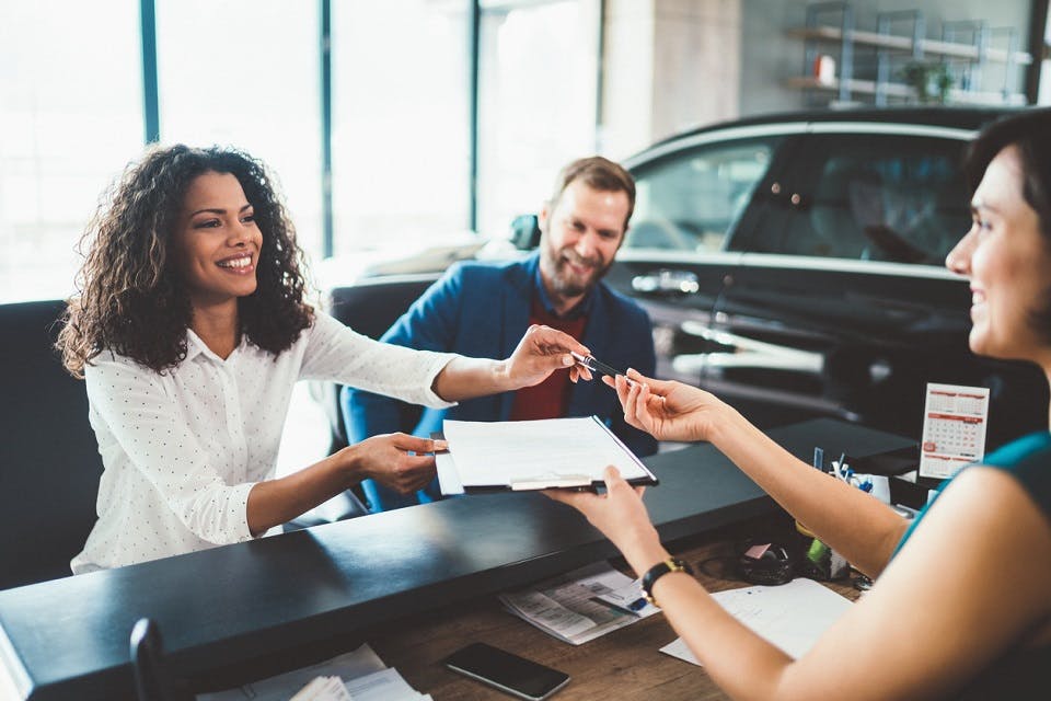 Couple in the showroom buying new car Young woman with her husband signing contract for buying a car