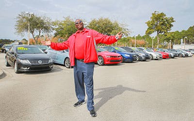 male car salesman in red shirt standing outside-min