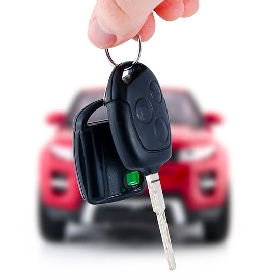 holding keys in hand with red vehicle in background