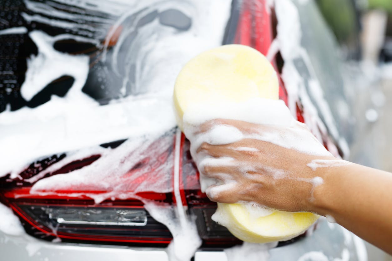 hand cleans car with soap and sponge