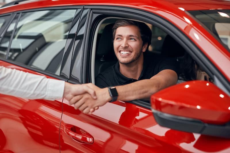 man in red car holding hand out window to shake hand