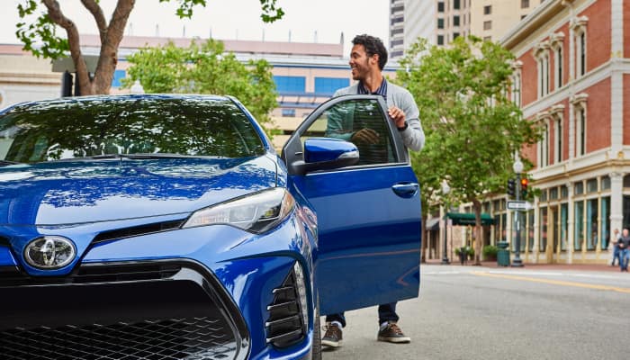 man getting inside a blue vehicle parked on street