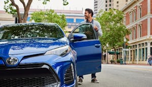 man getting inside a blue vehicle parked on street
