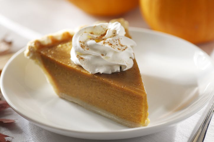 Pumpkin Pie With Whipped Cream A slice of pumpkin pie with whipped cream on top sprinkled with cinnamon.