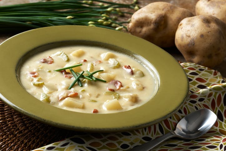 "Bowl of chunky potato soup prepared with idaho potatoes, bacon, celery, chives in a cream base."