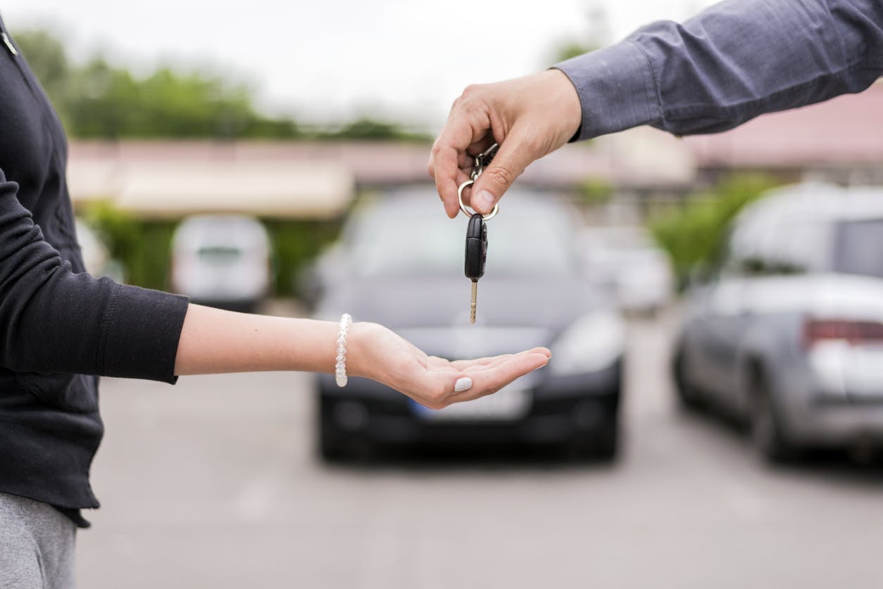 people exchange car keys in dealership lot