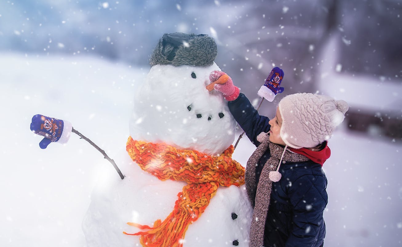 Child sculpts a snowman in a park