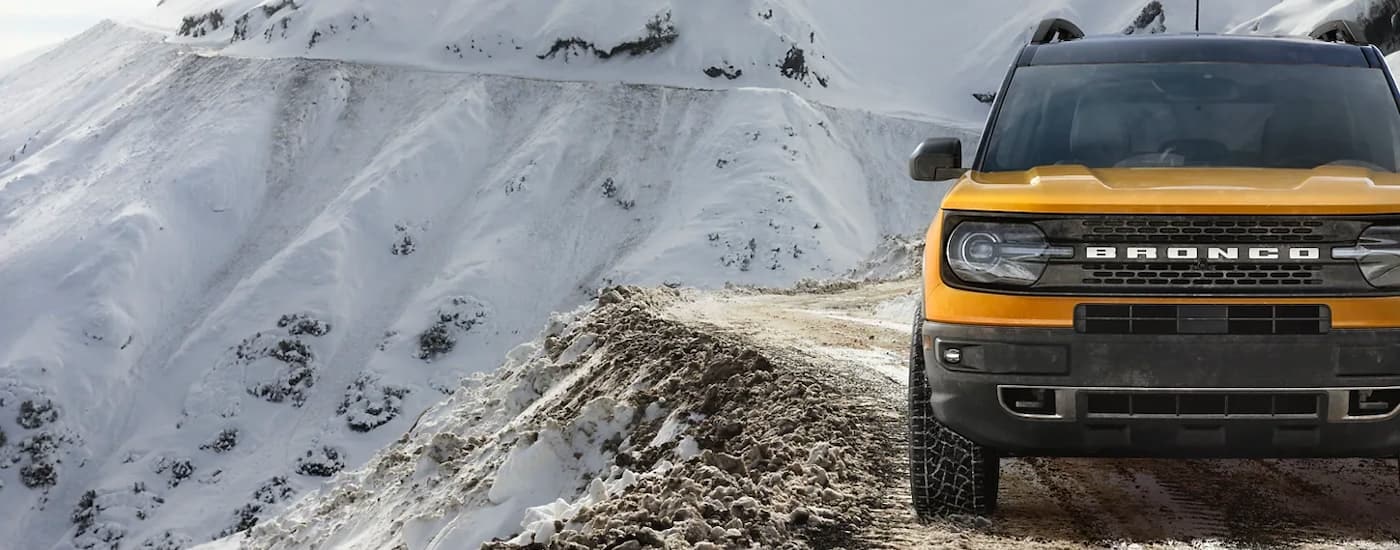 A yellow 2023 Ford Bronco Sport is shown driving on a snowy mountain trail.