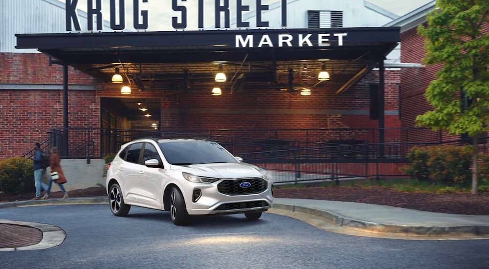 A white 2023 Ford Escape ST-Line is shown driving near a market after leaving a Ford dealer.