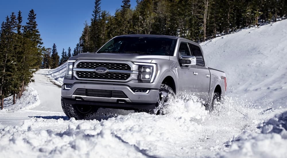 A silver 2023 Ford F-150 is shown driving through snow.