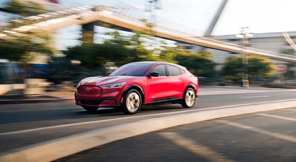 A red 2023 Ford Mustang Mach-E is shown driving on a city street.