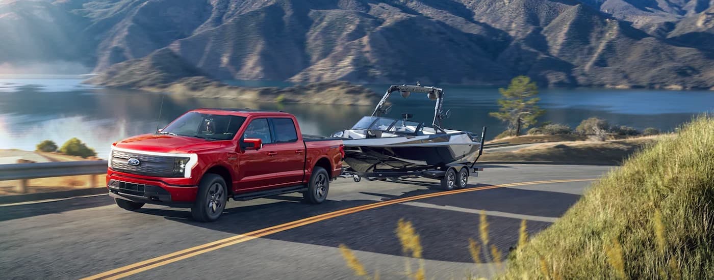 A red 2022 Ford F-150 Lightning is shown towing a boat past a lake after leaving a Ford dealer near you.