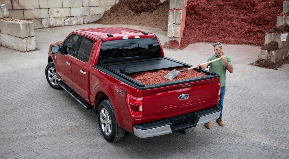 A man is shown loading a mulch into the bed of a red 2023 Ford F-150.
