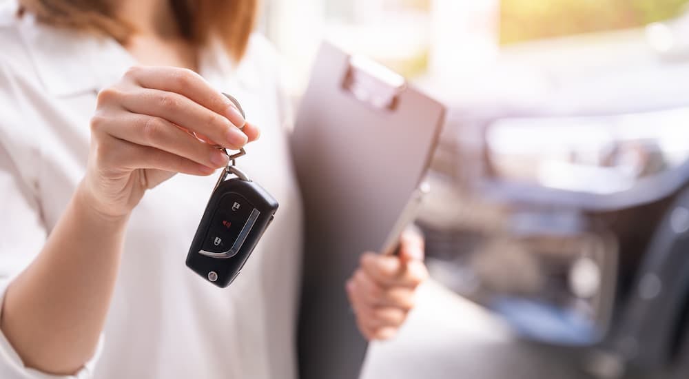 A car saleswoman is shown holding a key out at a dealership.