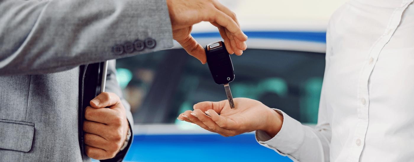 A car salesman is shown handing a key to a customer.