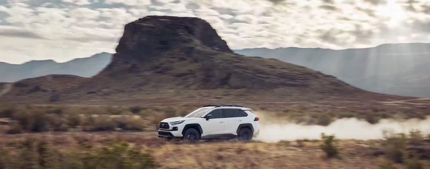 A white 2022 Toyota RAV4 is shown from the side while driving through a desert after leaving a used SUV dealer.