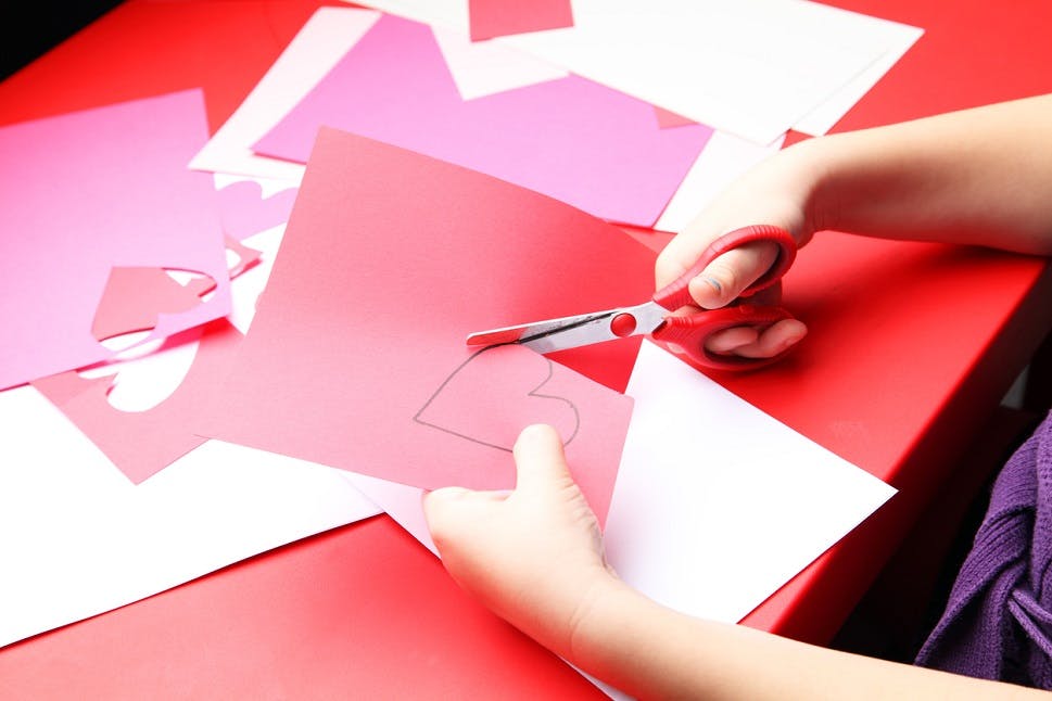A young girl cuts out a paper heart to use for her Valentine's Day card.