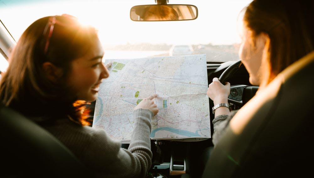 woman pointing at a map while friend is driving