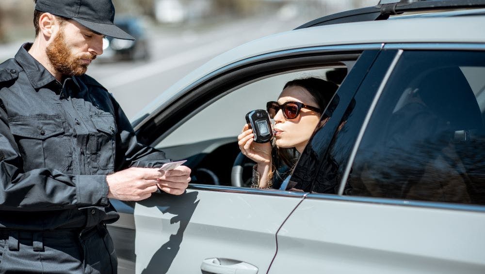 a woman taking a breathalyzer test inside her car in front of the police