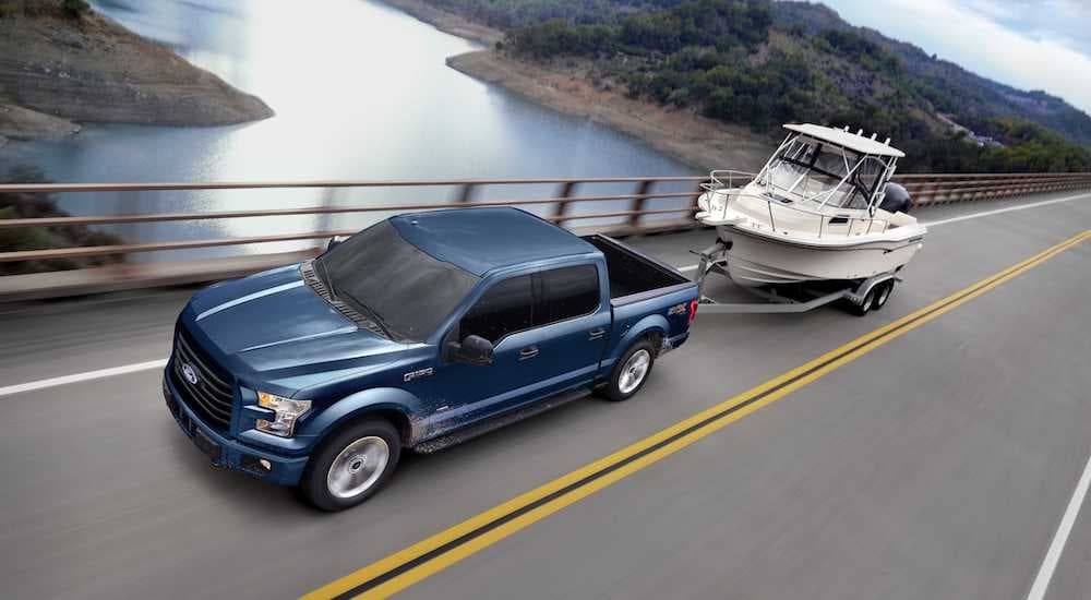 A blue 2017 Ford F-150 is shown towing a boat past a lake.