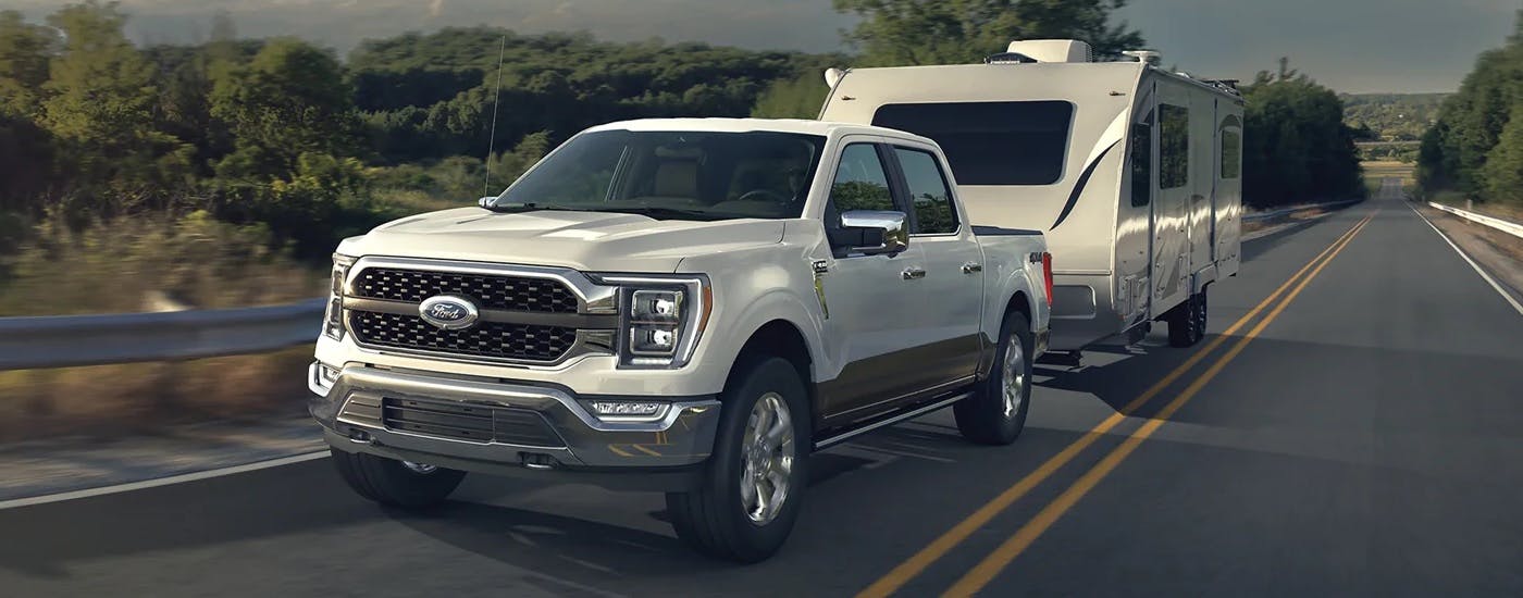 A white 2023 Ford F-150 is shown towing a trailer on an open highway.