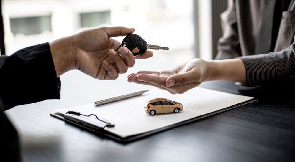 A close up shows people passing a car key.