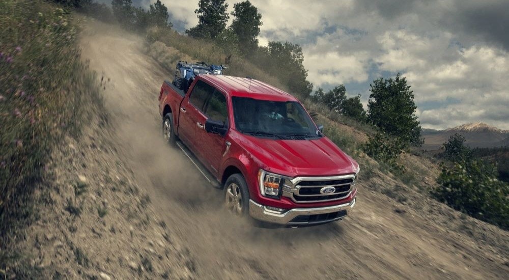 A red 2021 Ford F-150 is shown driving down a dusty trail.