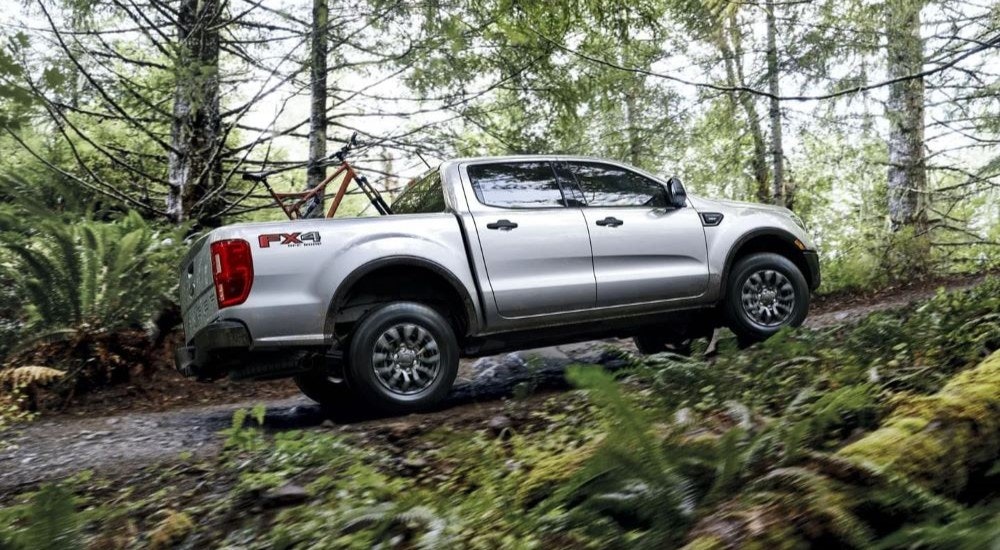 One of the most popular used Ford trucks for sale, a silver 2021 Ford Ranger XLT FX4, is shown on a trail in the woods.