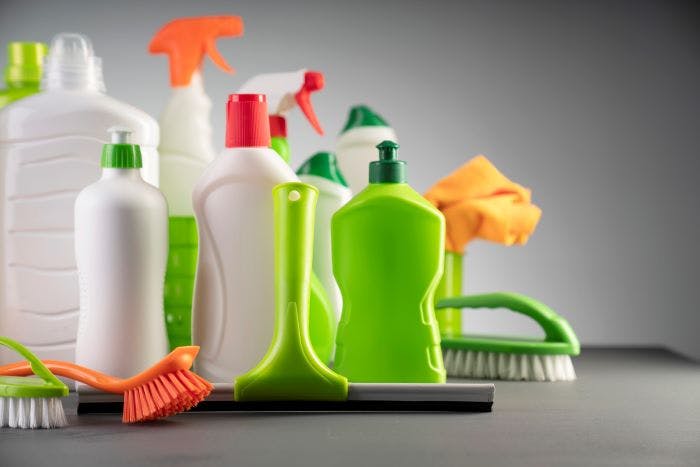 Green, white, and orange, cleaning bottles with a scrub brush and microfiber towel on a gray background