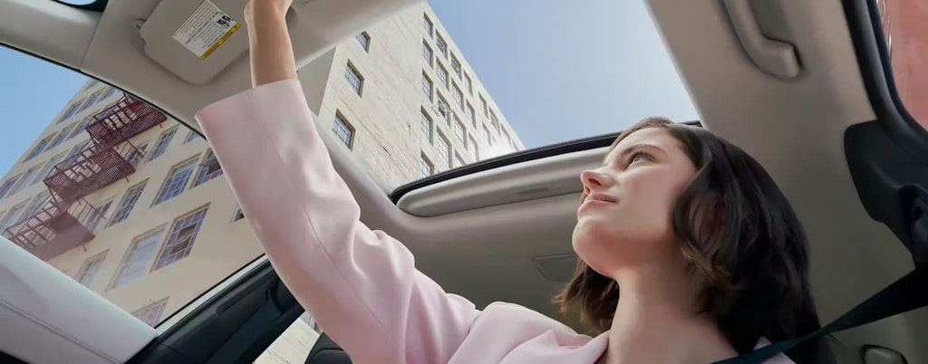 A woman is shown opening the sunroof in a 2023 Toyota Corolla Cross.