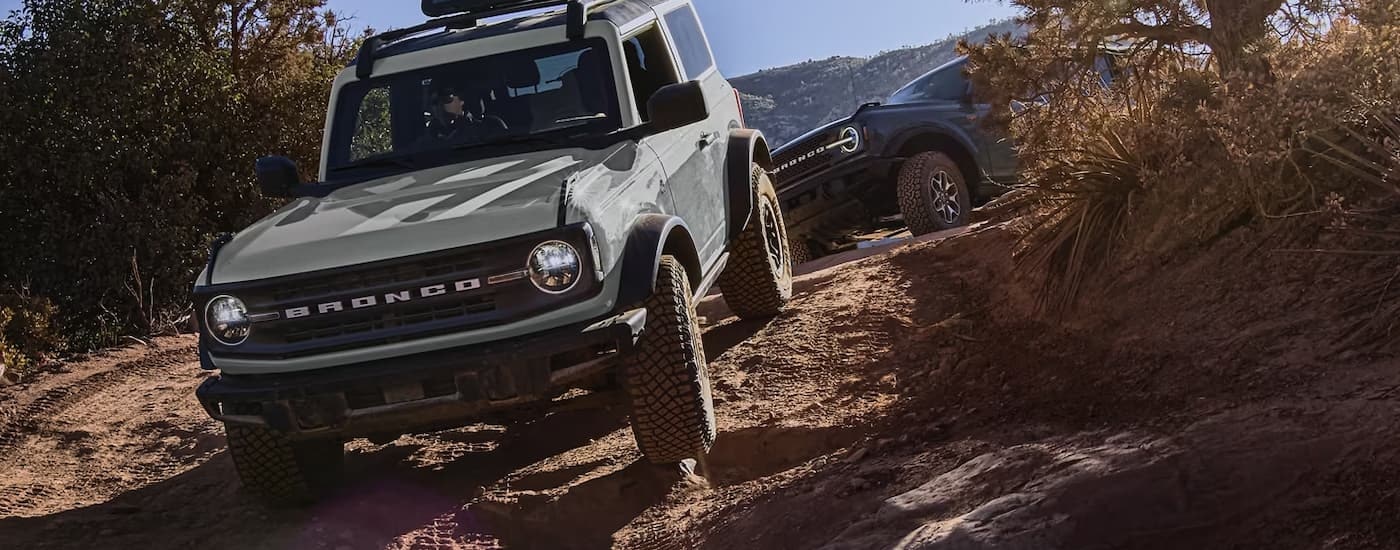 A grey and a black 2023 Ford Bronco are shown off-roading on a rocky trail.