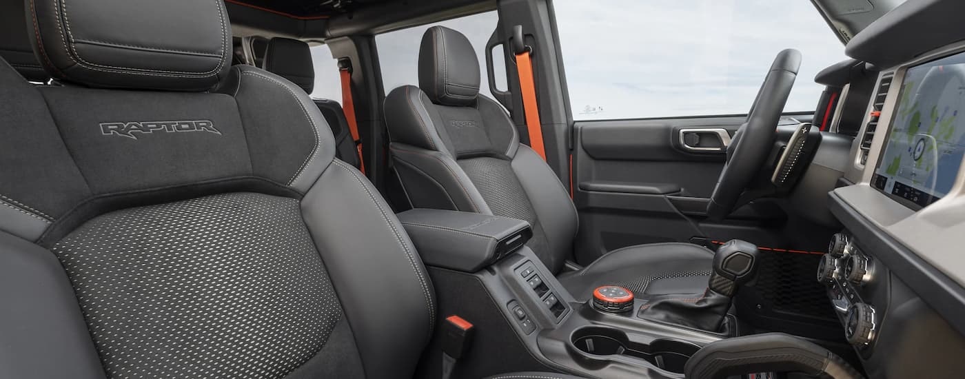 The grey and orange interior of a 2023 Ford Bronco Raptor shows the front seating and center console.