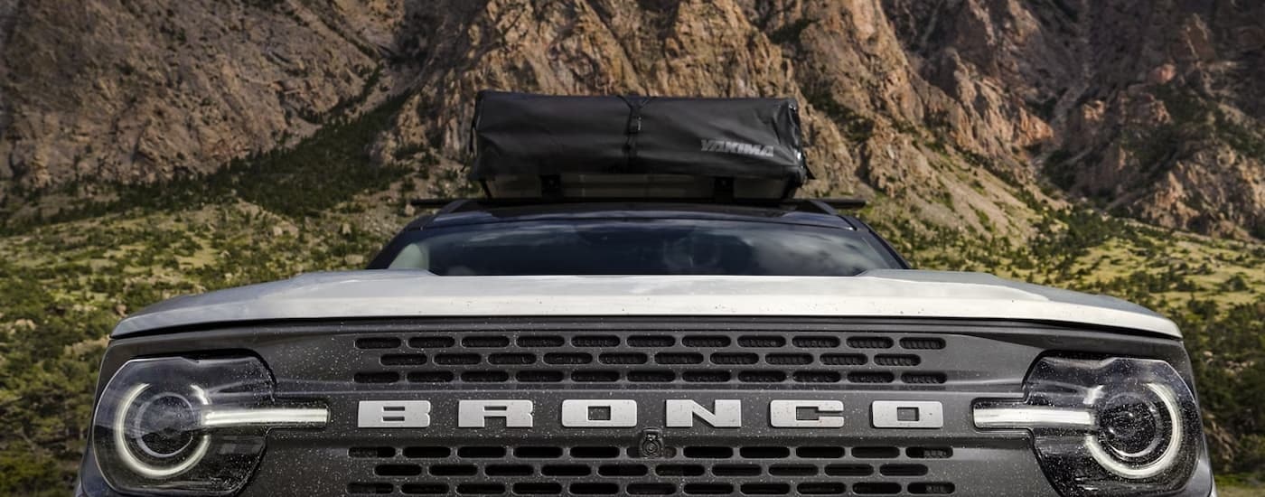 A close up of the grille of a white 2023 Ford Bronco Sport is shown in front of a rocky mountain view.